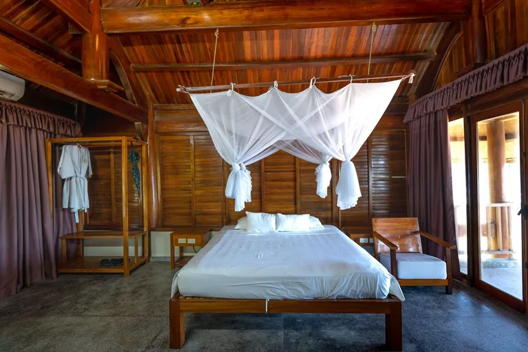 La chambre principale sous la charpente en bois précieux, lit à baldaquin